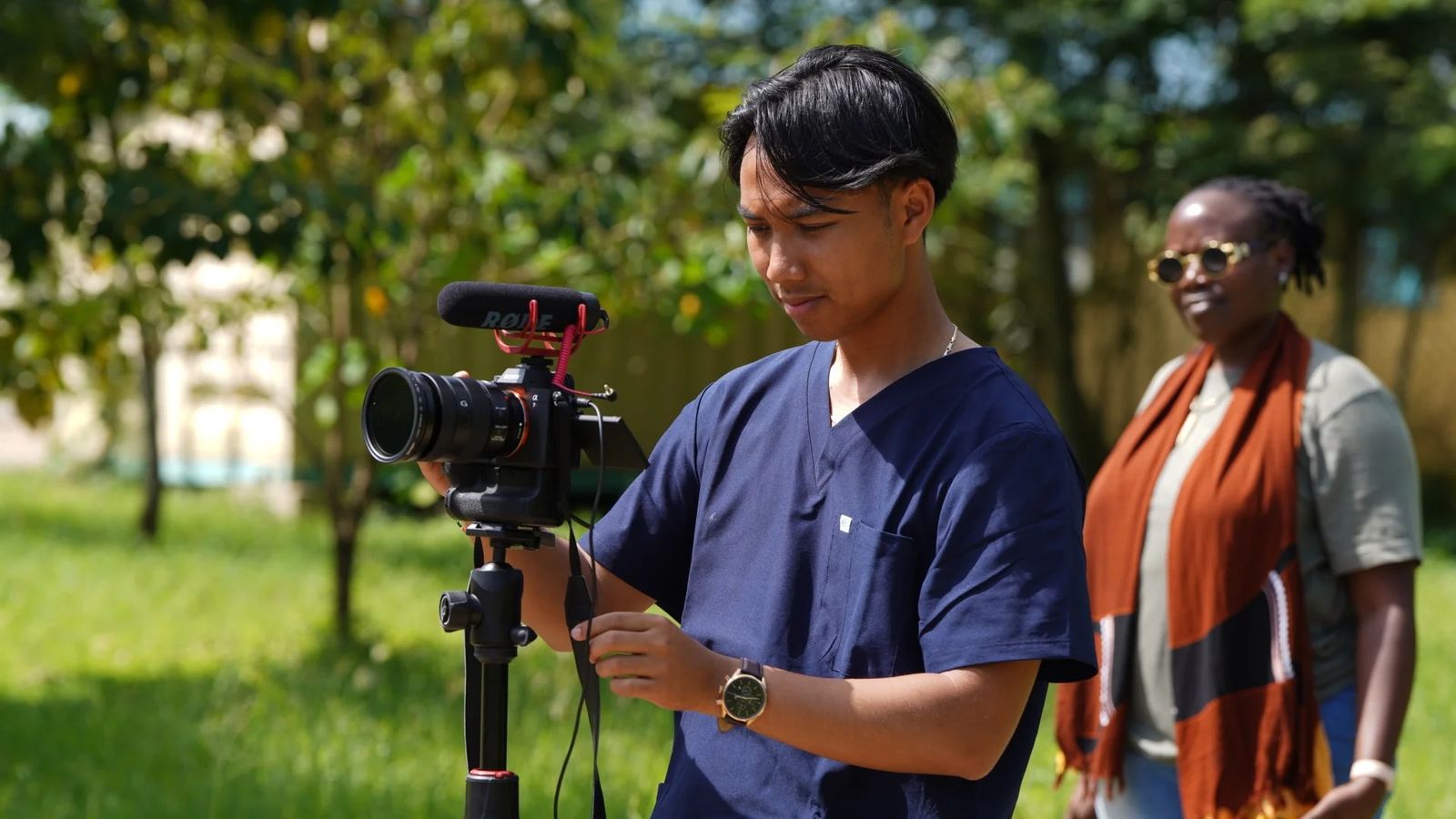 A filmmaker in scrubs recording at a clinic in Kenya