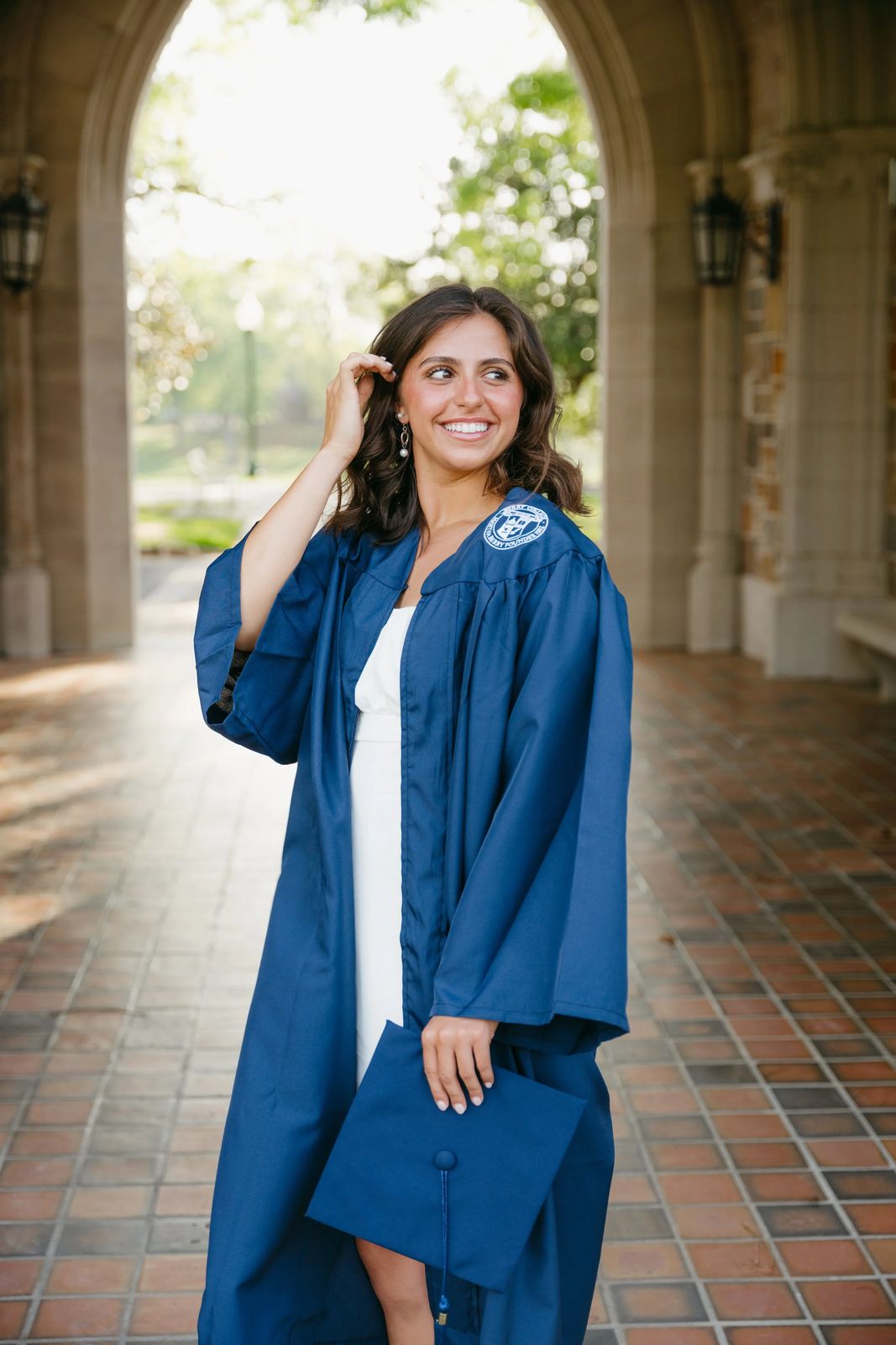 A senior in a cap and gown beneath a stone archway