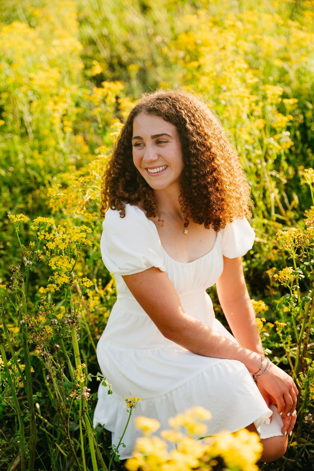 A senior in a white dress among yellow wildflowers