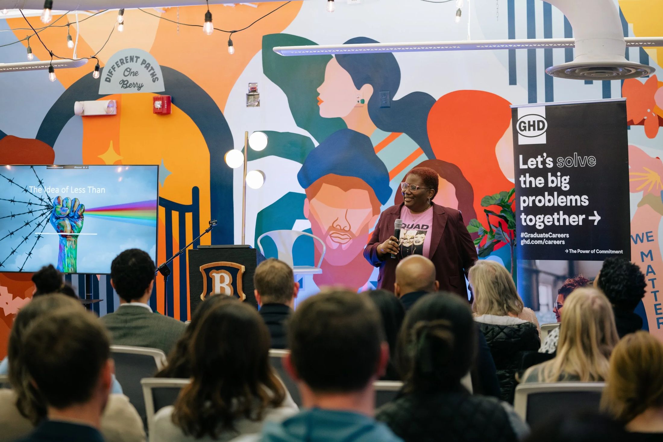 A speaker in front of a colorful mural at an event